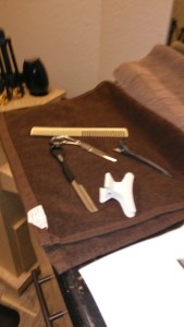 A brown towel holding two clips, a comb, a pair of scissors and a haircutting razor.