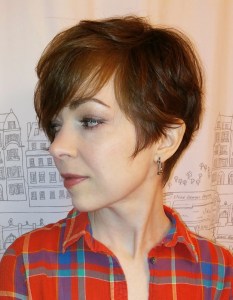 Woman wearing a plaid shirt. She has a long pixie haircut shown from the side front.