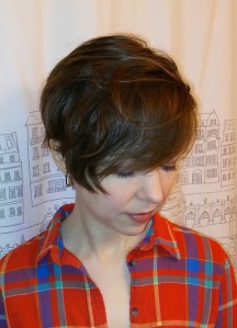 Woman wearing a plaid shirt. She has a long pixie haircut shown from the top front.